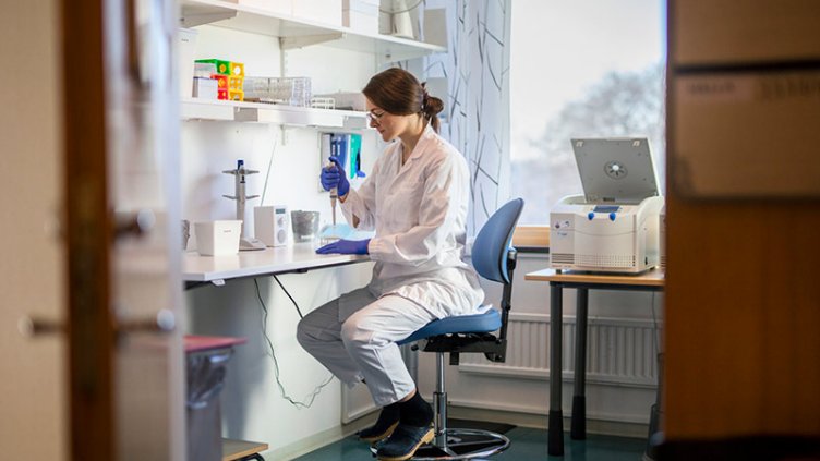 Portrait of a young woman wearing glasses and a lab coat. She is working in a life sciences lab and holding a syringe.