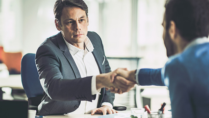 Mid adult insurance agent shaking hands with his customer in the office.