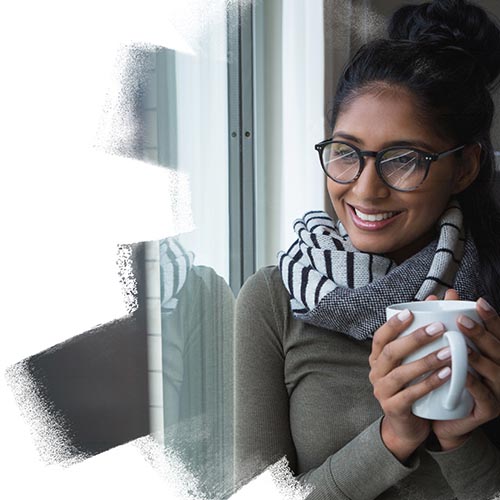 Indian women with a mug watching outside the window and smiling