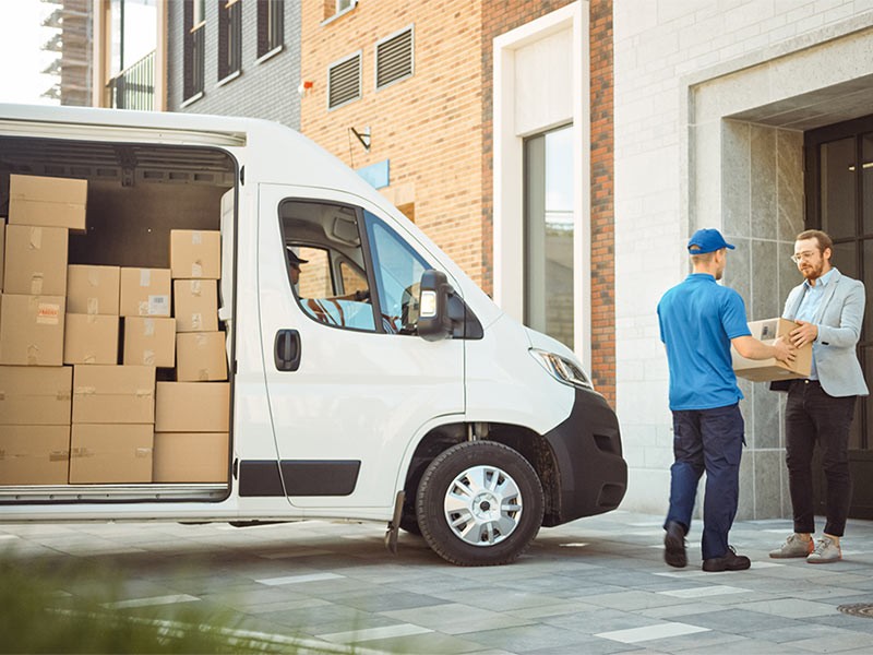 Delivery Man Gives Postal Package to a Business Customer, Who Signs Electronic Signature POD Device. In Stylish Modern Urban Office Area Courier Delivers Cardboard Box Parcel to a Man