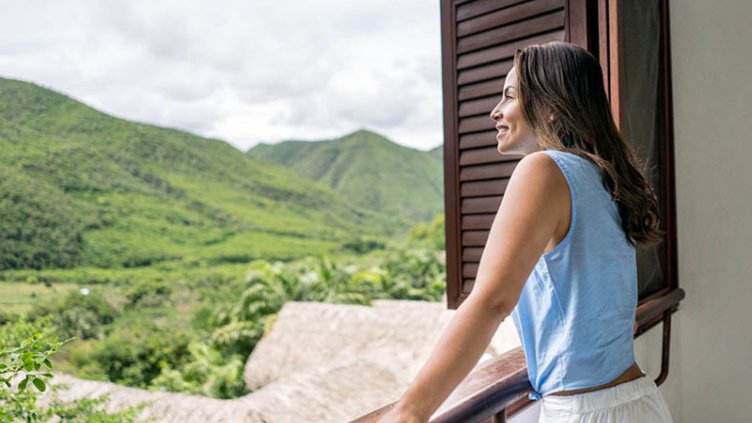 A woman with a smile on her face is enjoying the view of mountain scenery through a window.