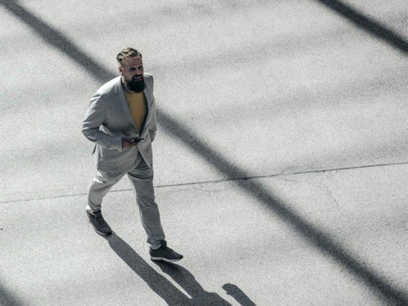 A man walking by as his shadow reflects ahead of him