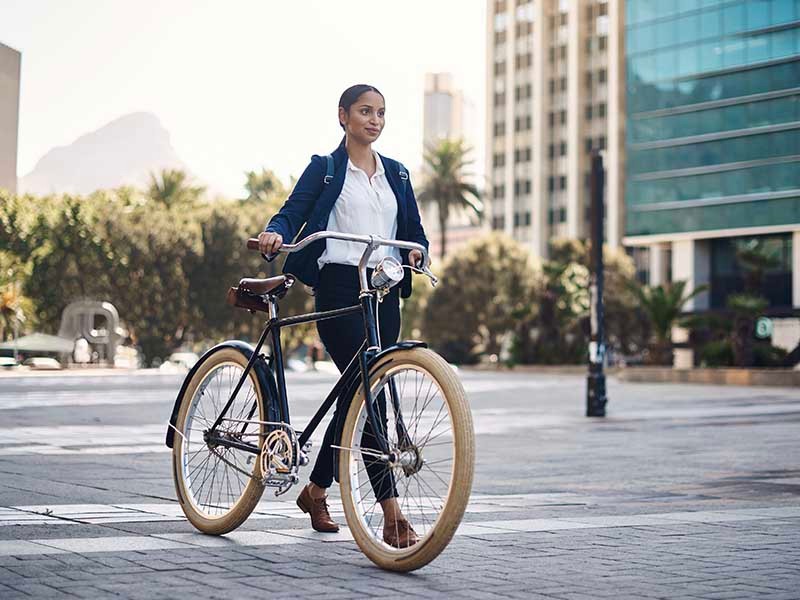 Young woman walking by with a bicycle in front of a commercial building