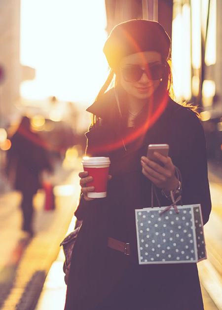 Young woman looking at her phone screen with a cup of coffee in the other hand