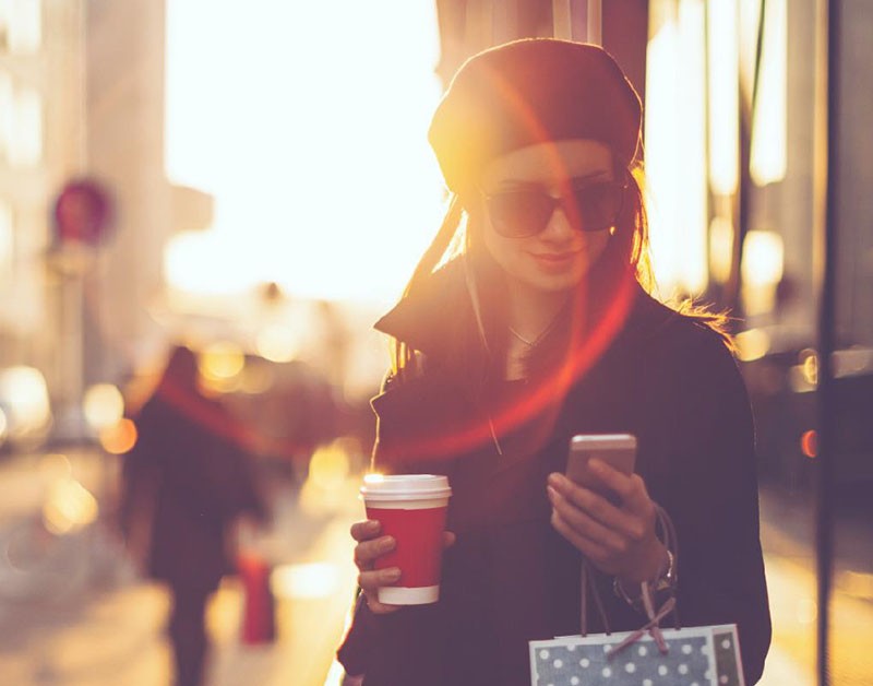 Young woman looking at her phone screen with a cup of coffee in the other hand