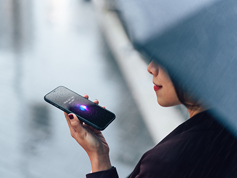 Close up shot of young Asian businesswoman talking to virtual assistant on smartphone in the rain.