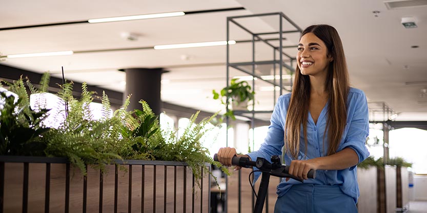 Happy businesswoman leaving the office with a push scooter