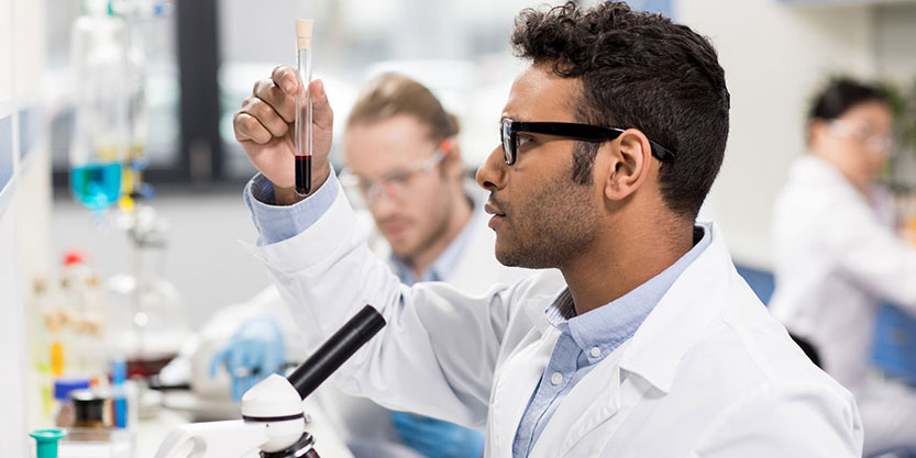 Side view of young scientist in eyeglasses looking at test tube in research laboratory