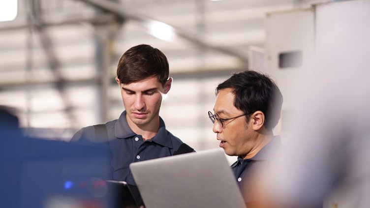 Men looking at computers discussing content while standing in manufacturing space.