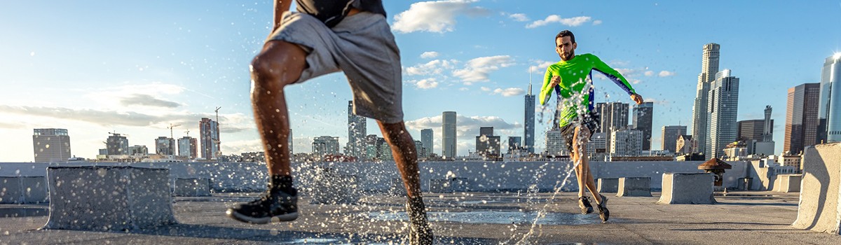 Two men jogging on a wet strech in the front of high rise buildings