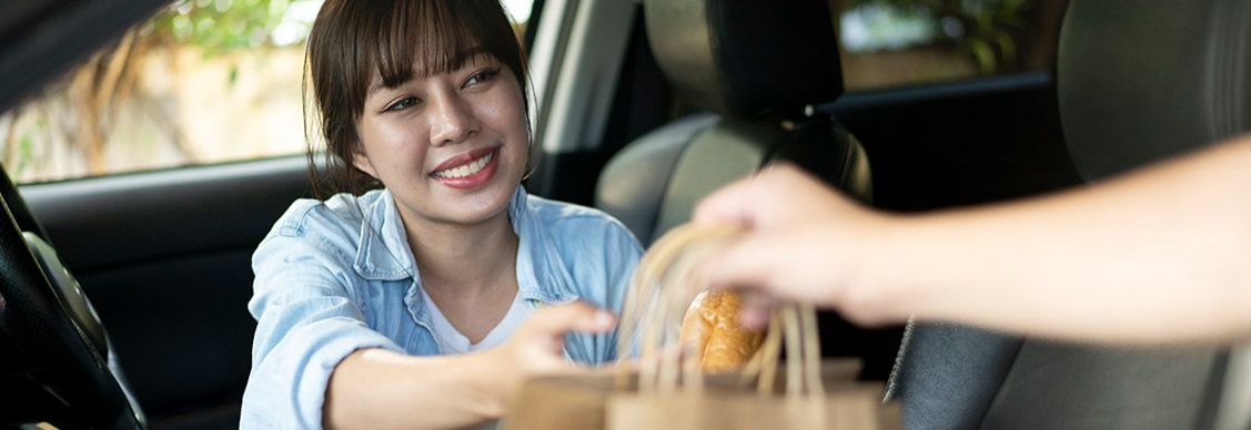 Young woman smiles as she gets food on the way into the car