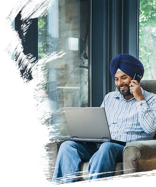 A male employee sitting on sofa and working on laptop, laughing while speaking on phone